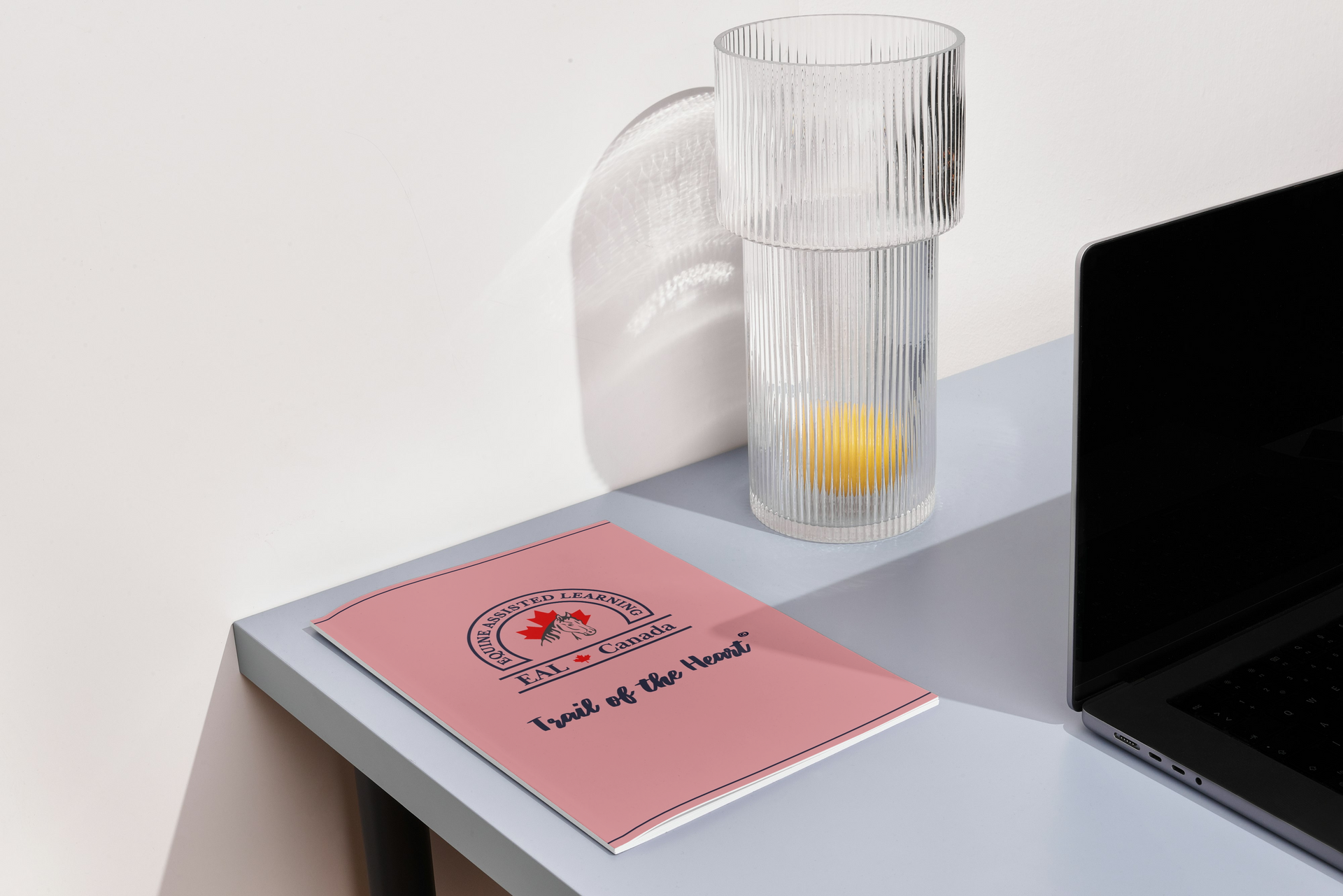 A notebook is sitting on a desk next to a glass of water and a laptop.