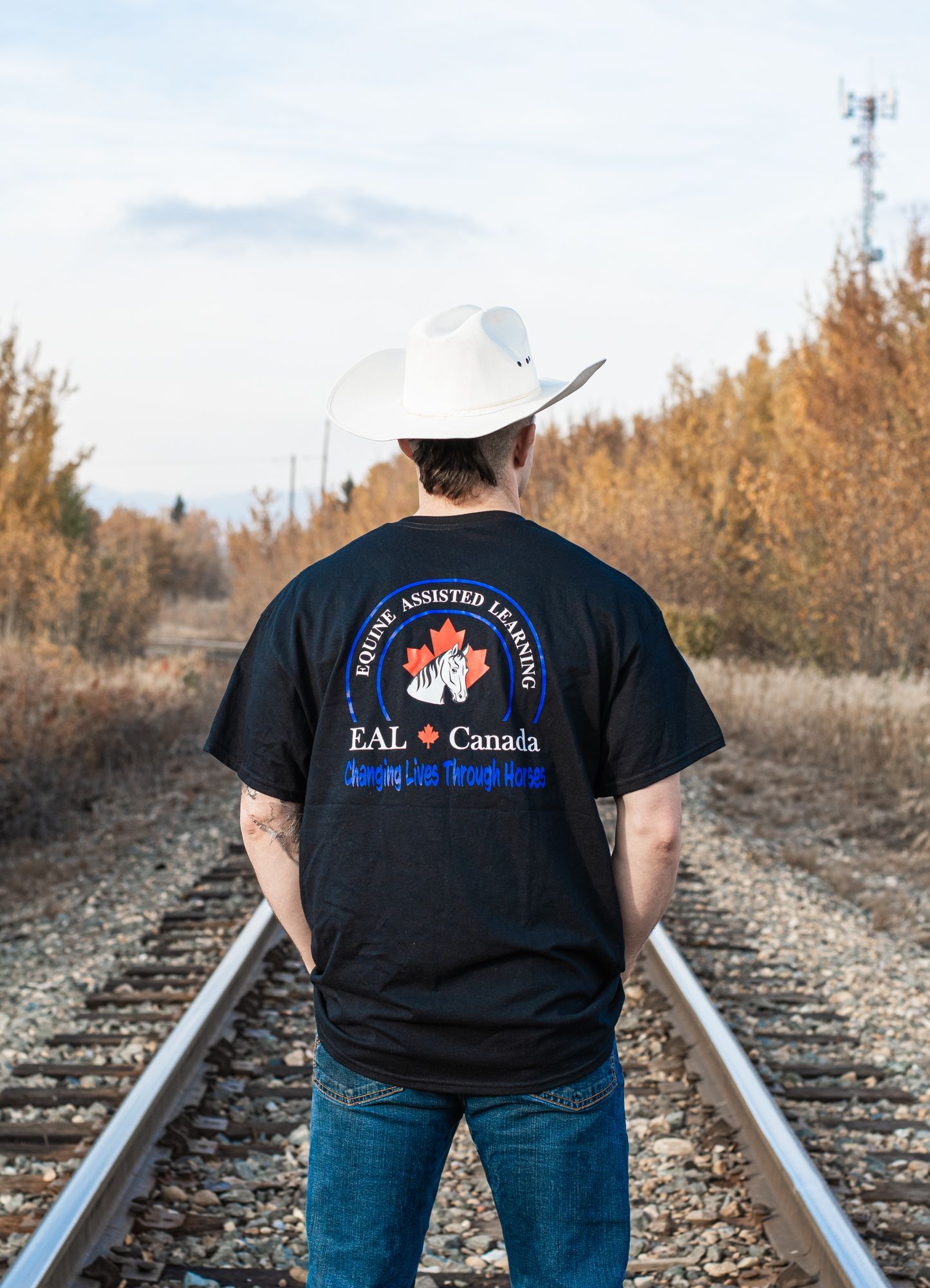 A man wearing a cowboy hat and a black shirt is standing on train tracks.