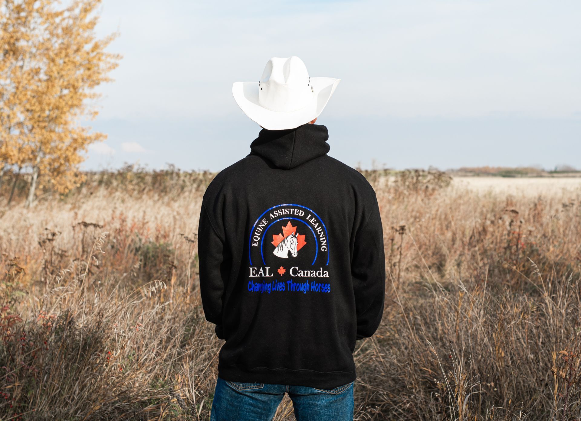 A man wearing a cowboy hat and a black hoodie is standing in a field.