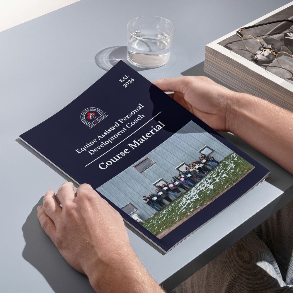 Hands holding open a course material booklet, titled "Equine Assisted Personal Development Coach."