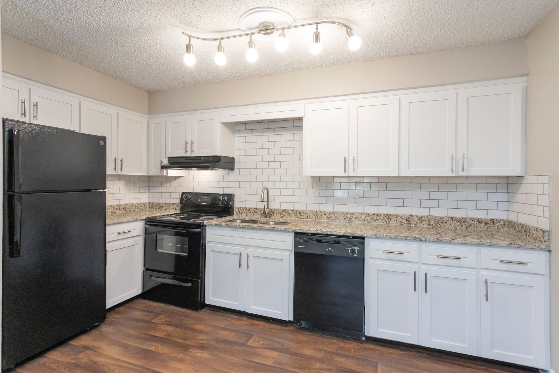 Modern kitchen with white cabinets, granite countertops, black appliances, and a subway tile backsplash.