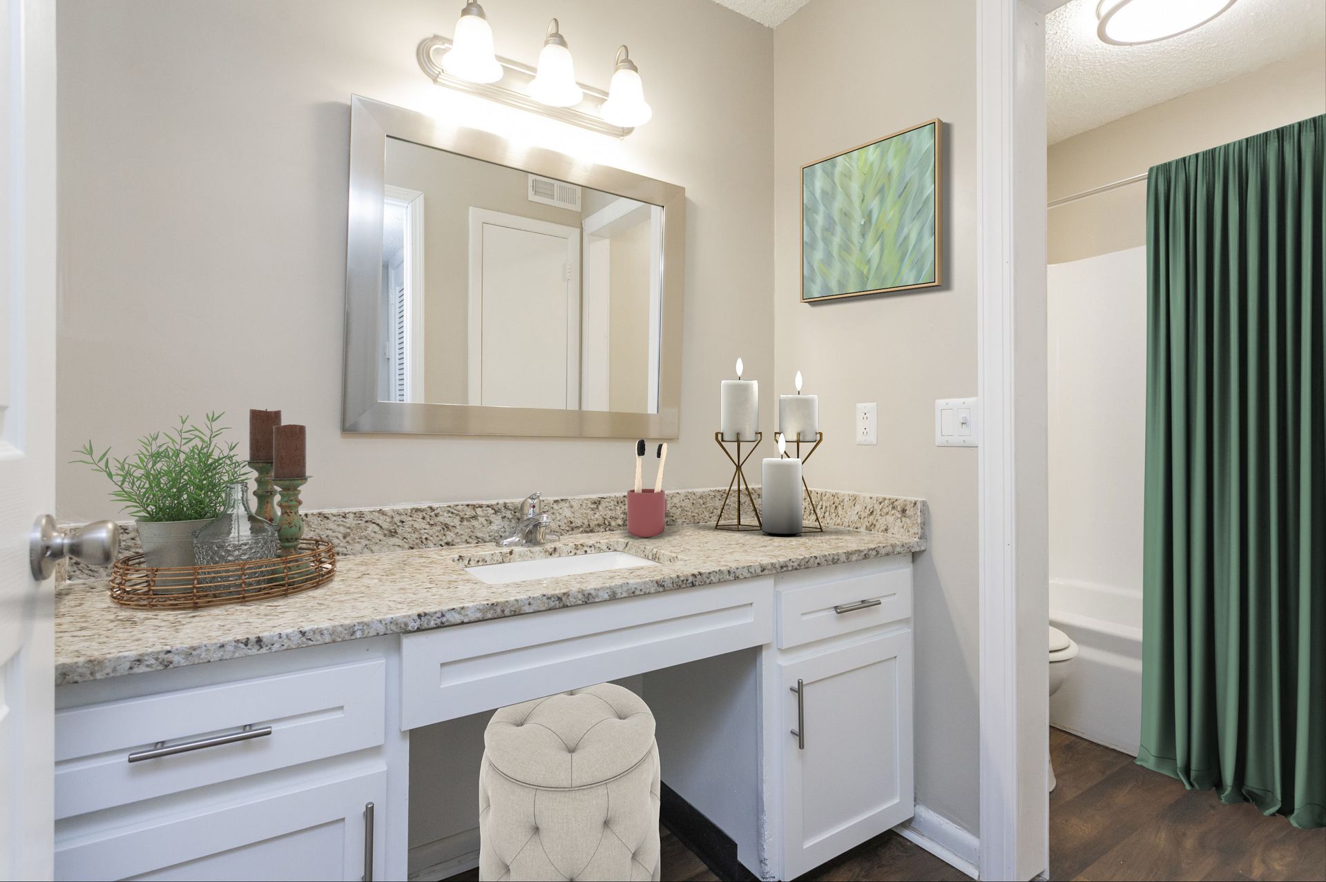 A bright bathroom vanity with white cabinets, speckled granite countertops, a framed mirror, and a green shower curtain.