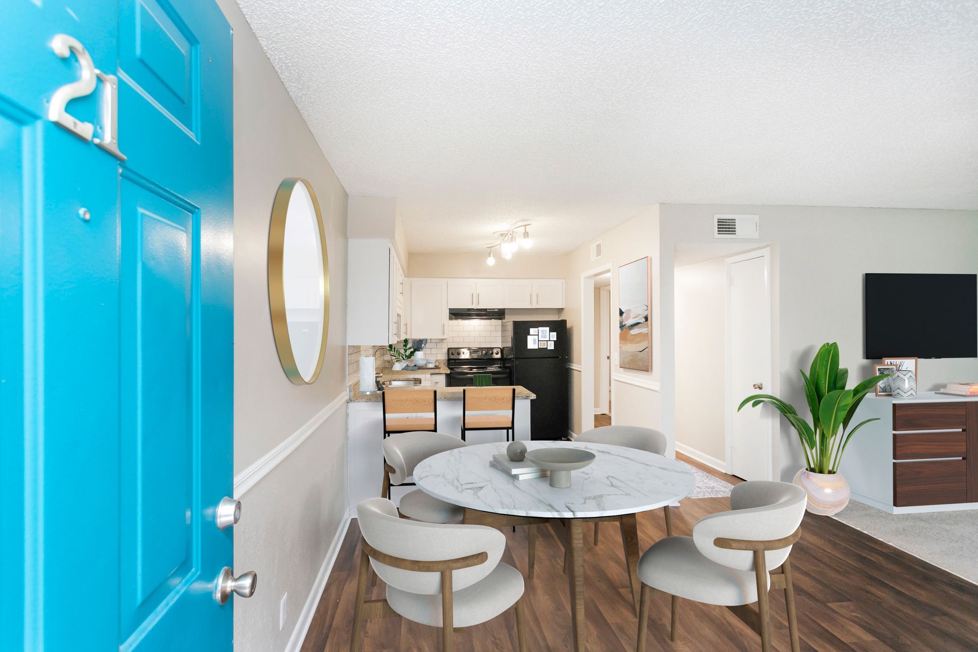 A bright apartment entryway opens into a dining area with a round white marble table, chairs, and a kitchen background.