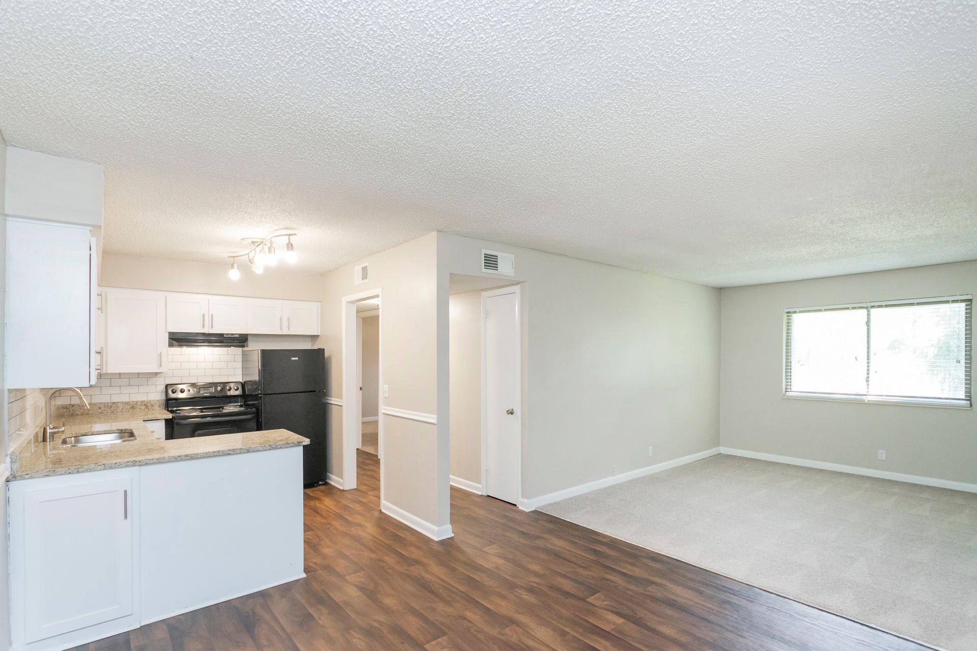 An open-concept kitchen and living area with white cabinets, dark countertops, dark wood flooring, and light gray walls.
