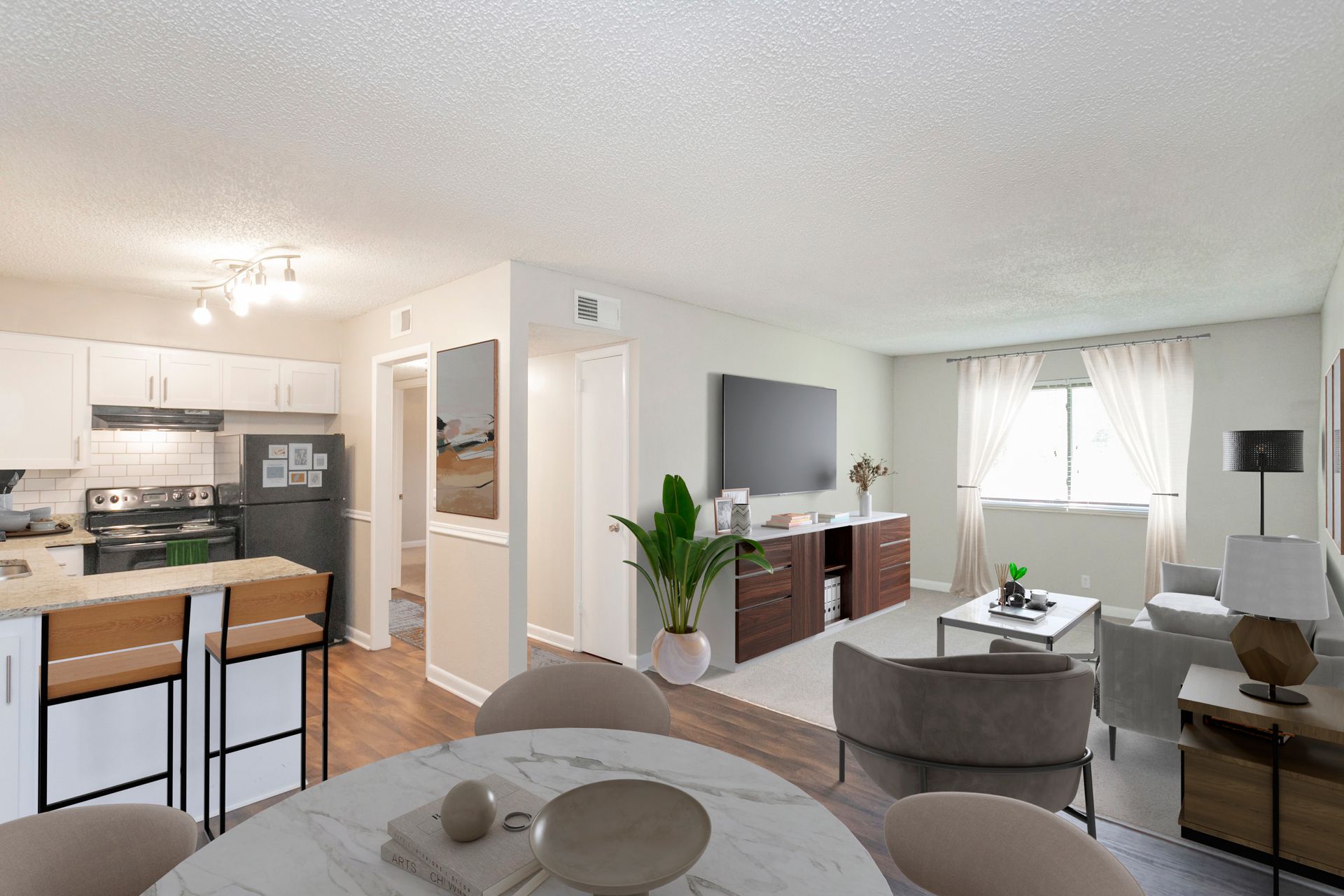 A well-lit, open-concept living area featuring a kitchen with a bar, a dining table, and a cozy living room with a TV.