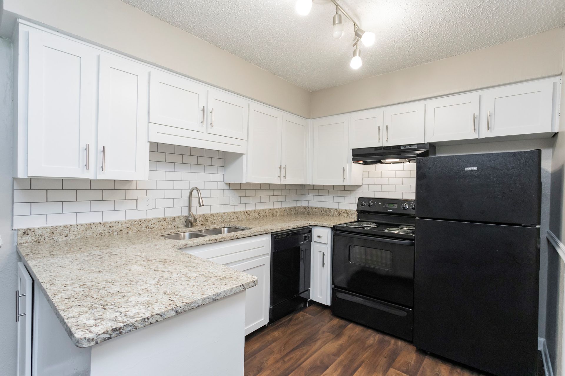 A kitchen with white cabinets, granite countertops, subway tile backsplash, and black appliances on a wood-look floor.