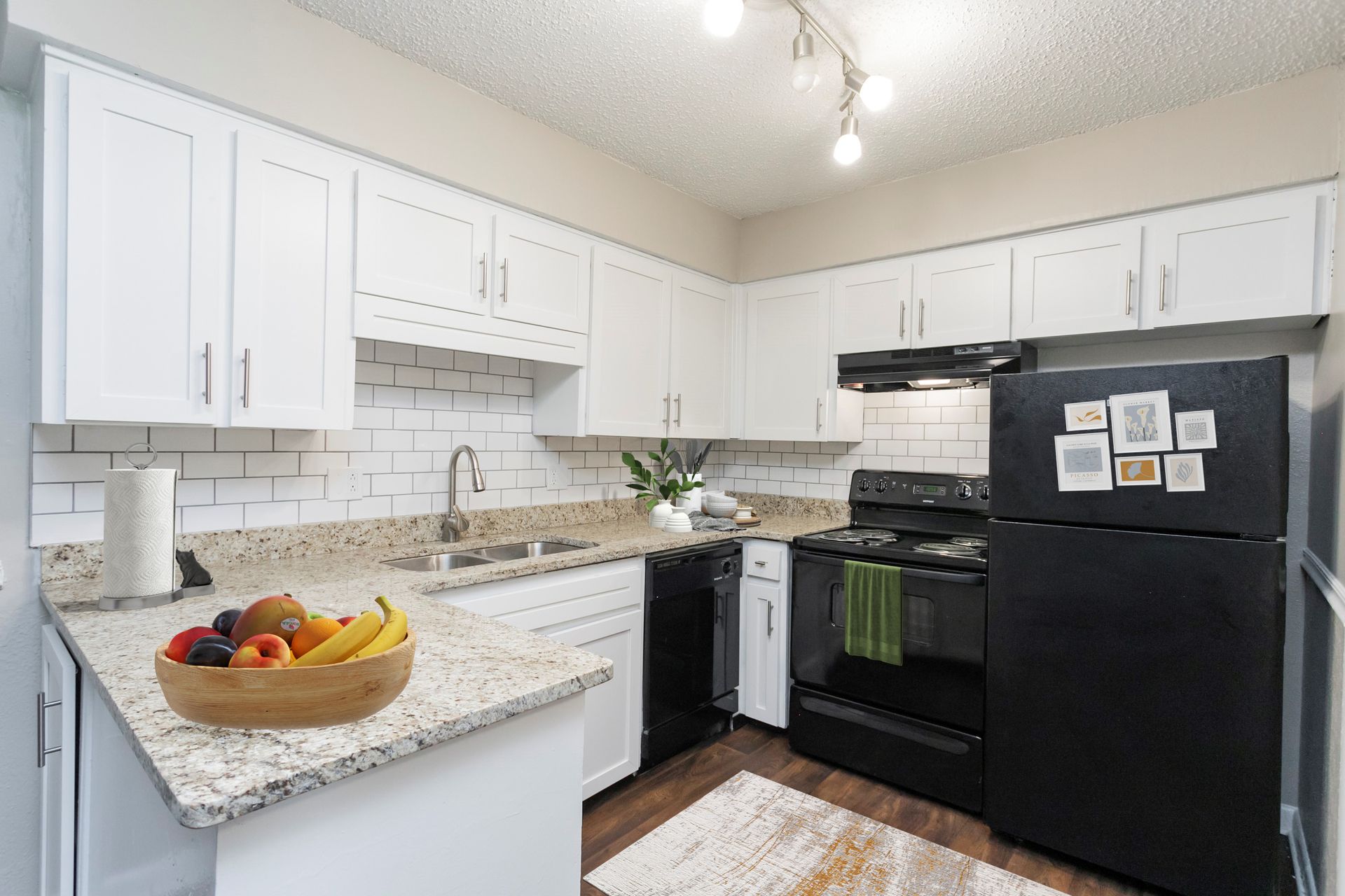 Kitchen with white cabinets, granite countertops, subway tile backsplash, and black appliances.