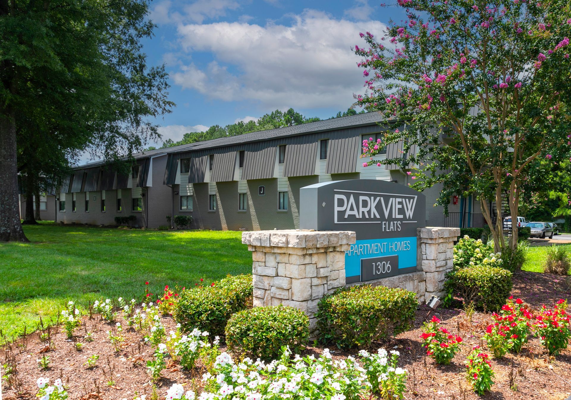 A two-story apartment complex named Parkview Palms with a stone monument sign, green lawn, and flower beds in front.