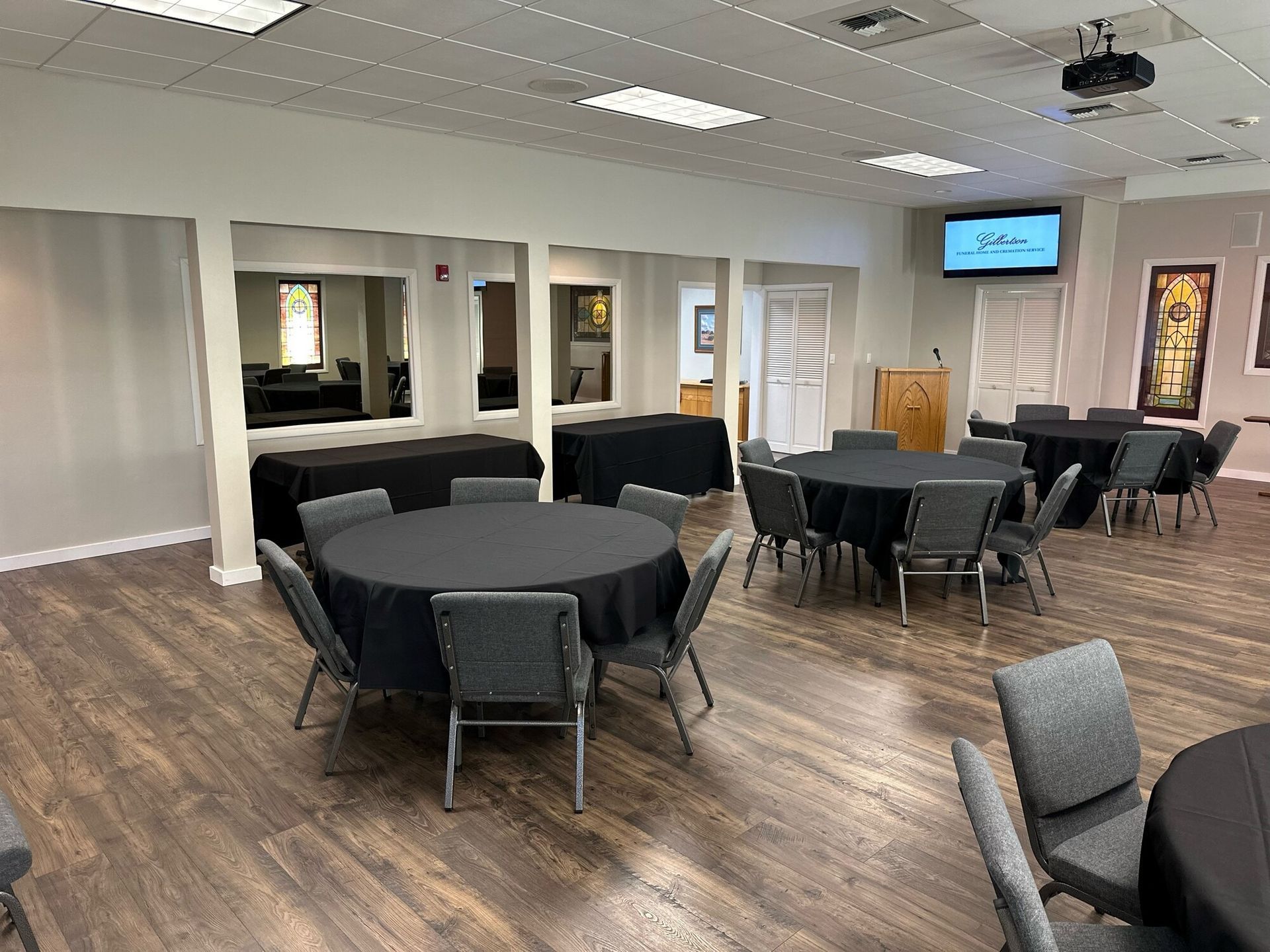 Event room with round tables draped in black, gray chairs, and hardwood floors.