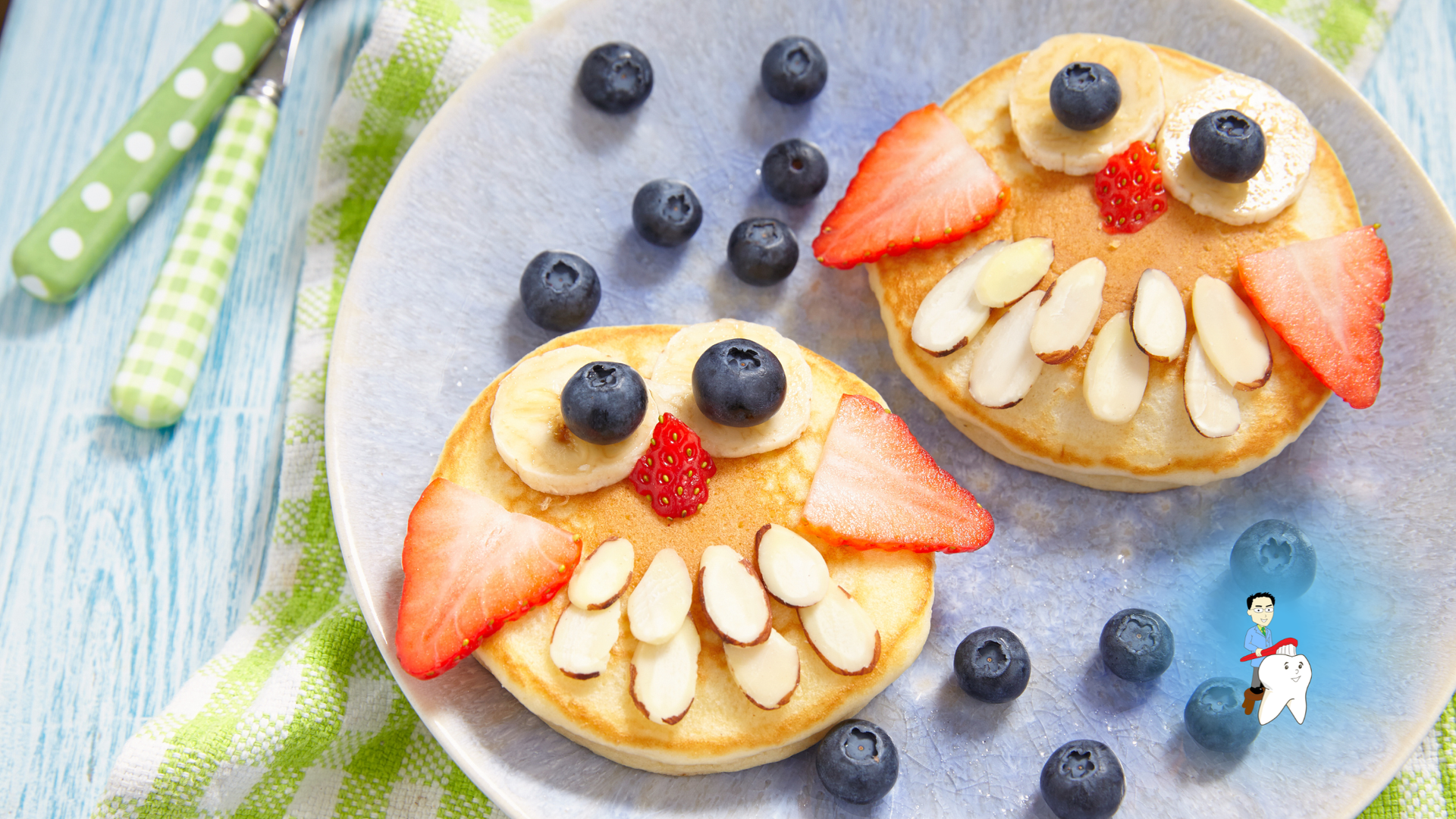 Three fruit pancake faces on a plate with berries, banana slices, and strawberry slices