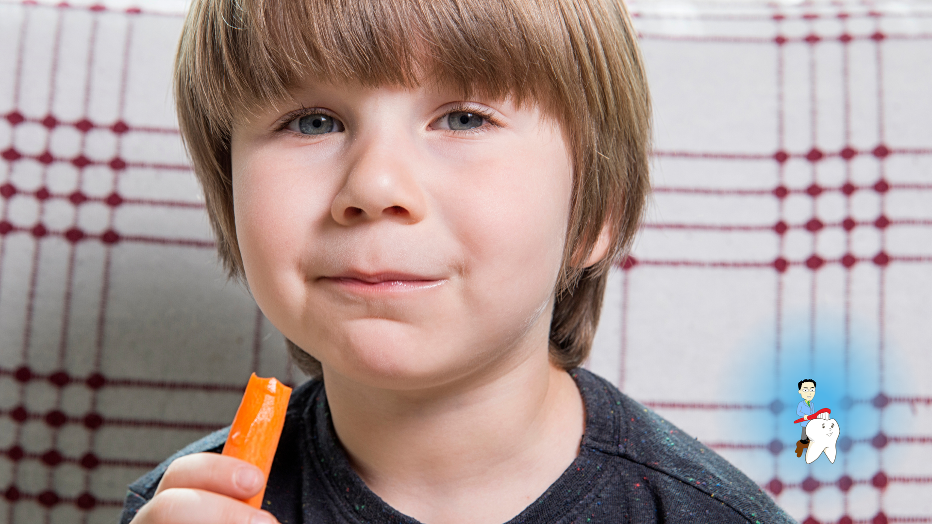 Young child holding an orange popsicle in front of a checkered curtain