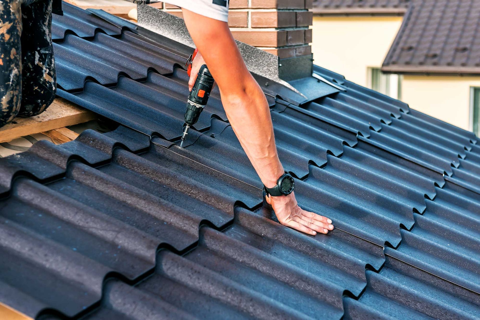 Roof installer using power drill to secure metal roofing tiles during residential roof installation.