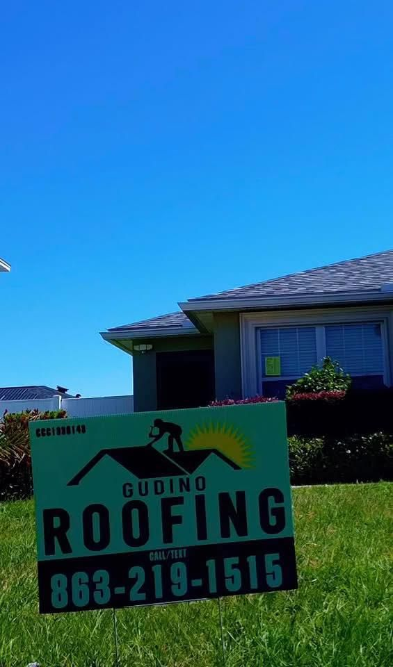 Roofing yard sign in front of a house under a bright blue sky, reading “Gubino Roofing” and 863-219-1515