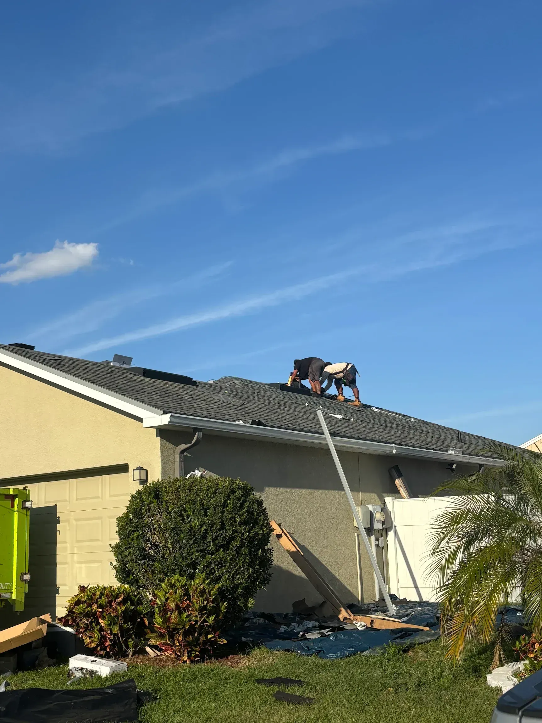 Two workers on a roof repairing tiles with a ladder leaning up the house