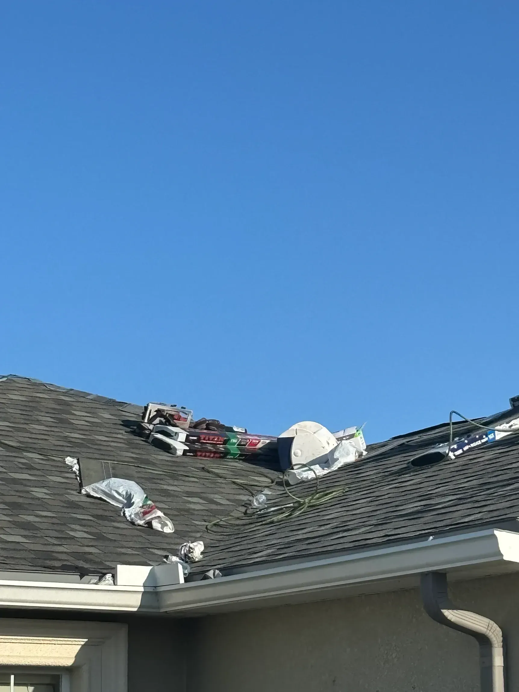 Rooftop with several scattered items, including a white satellite dish, against a blue sky.