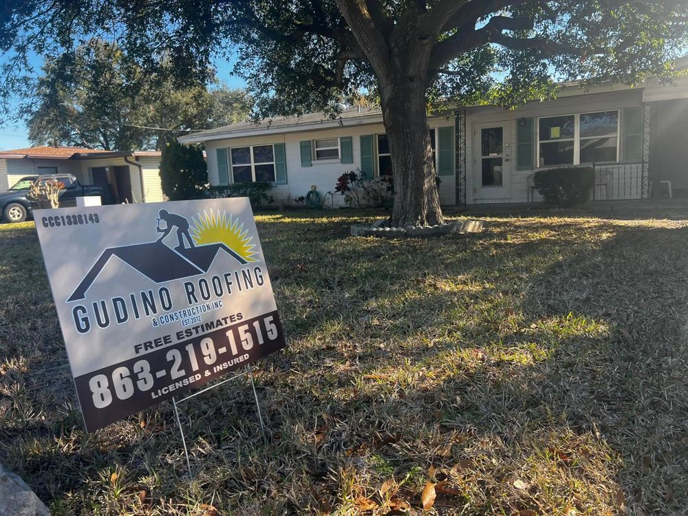 Lawn sign for “Gudino Roofing” in front of a suburban house with a large tree and yard.