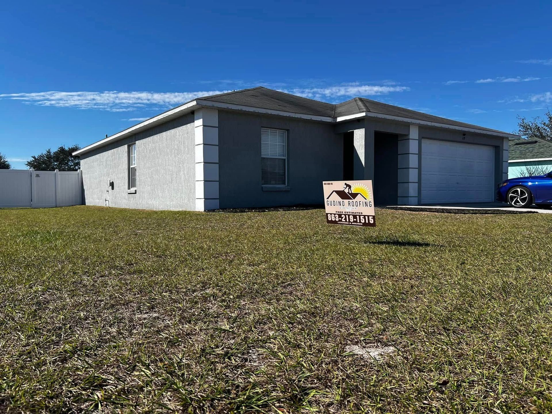 Single-story gray house with a front lawn under a blue sky, for sale sign in the yard.