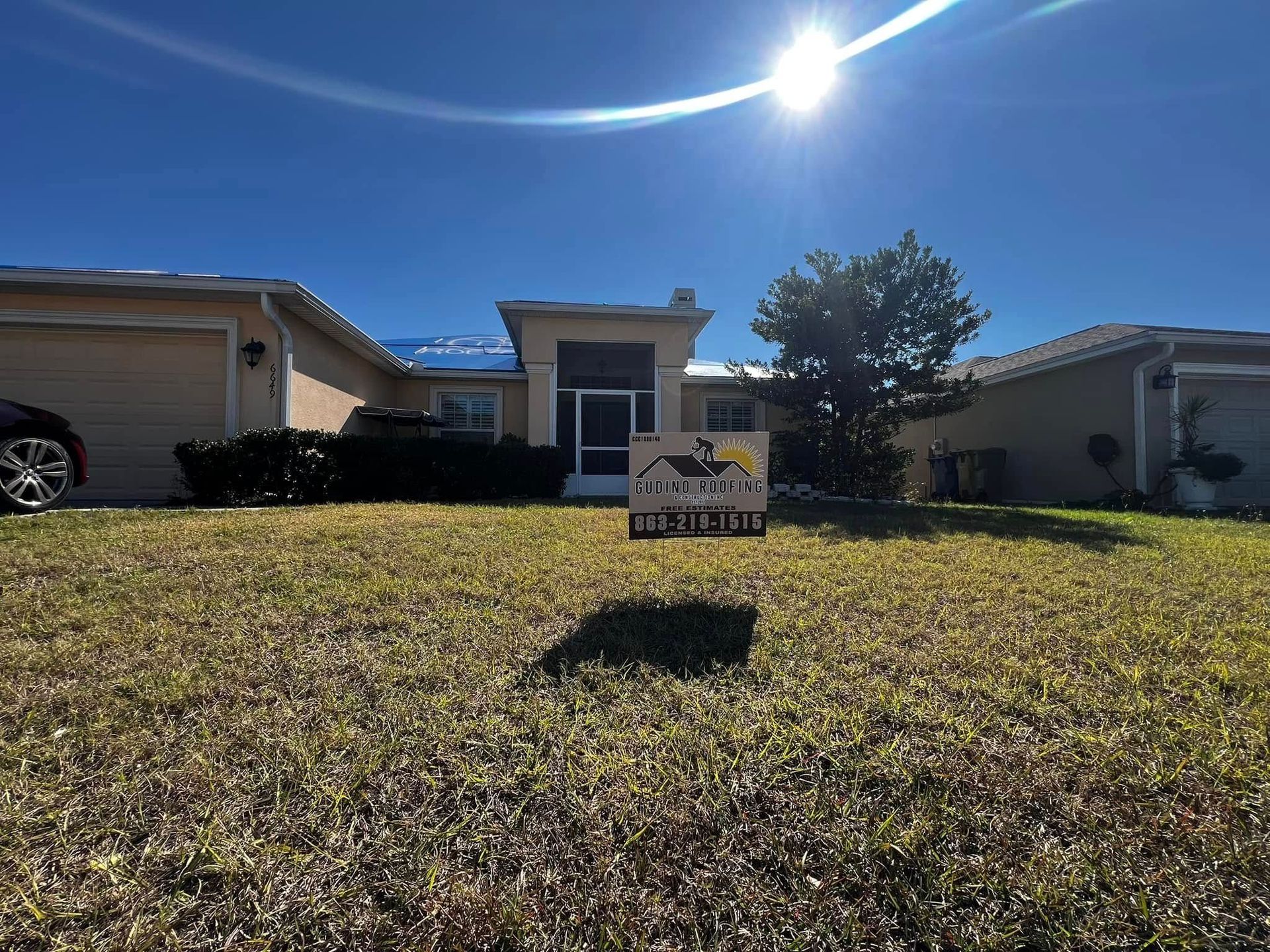 Sunlit suburban house with a lawn sign in the front yard under a bright blue sky
