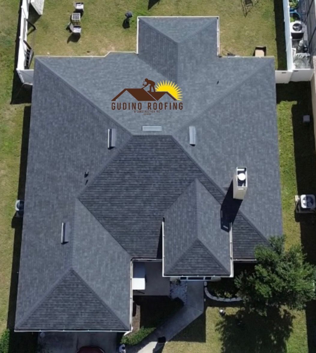 Aerial view of a gray-roofed house with a logo painted on the roof and a small yard around it
