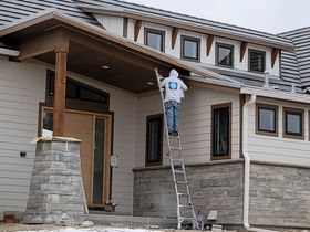 A man is painting a house with a bucket of paint.