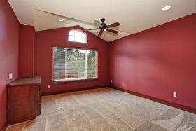 An empty bedroom with red walls and a ceiling fan.
