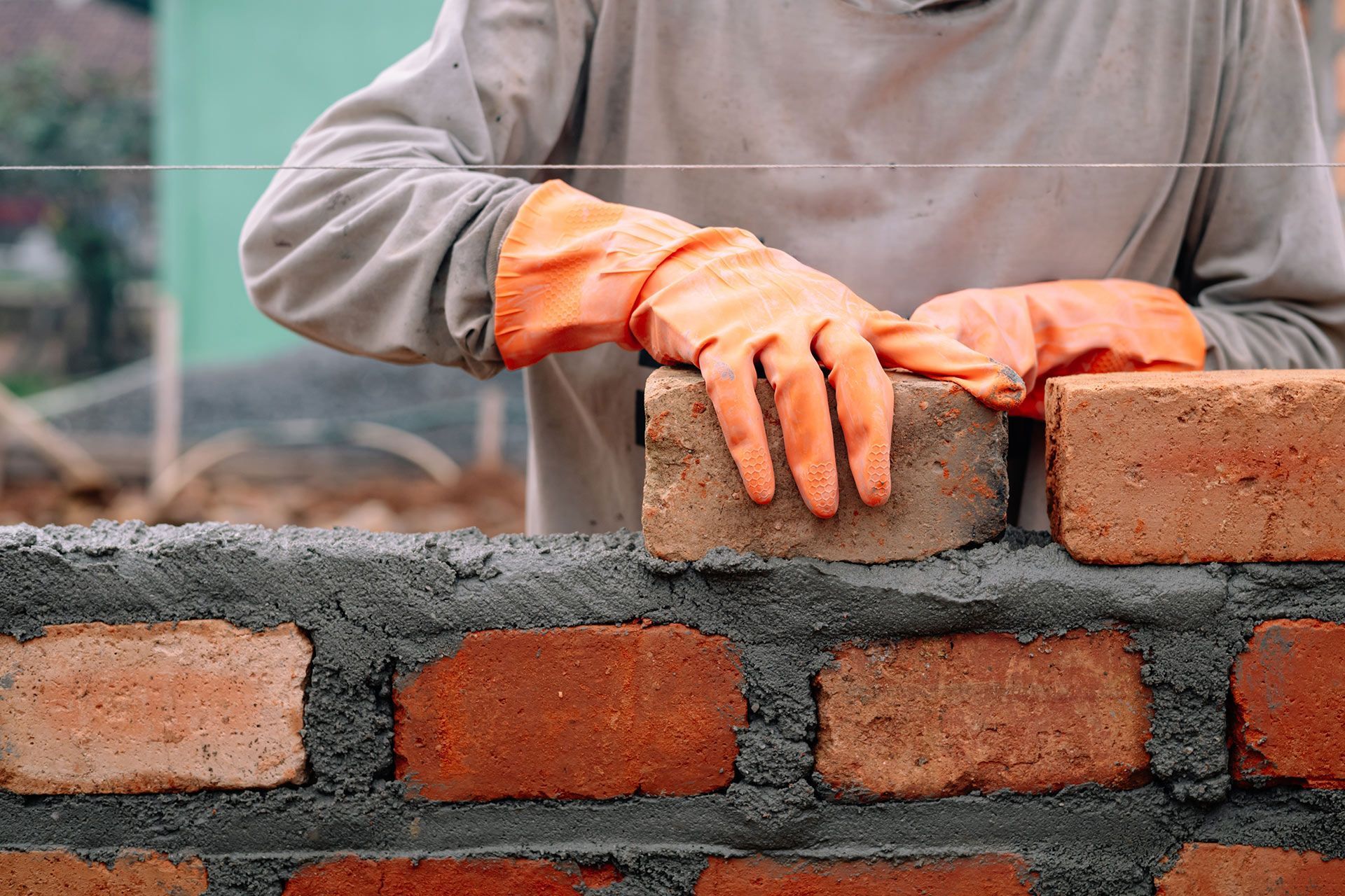 Hands in orange gloves laying bricks on a partially built wall