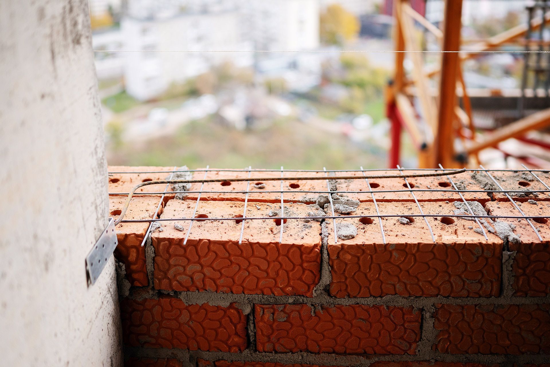 Partially built red brick wall on a construction site, with blurred buildings in the background