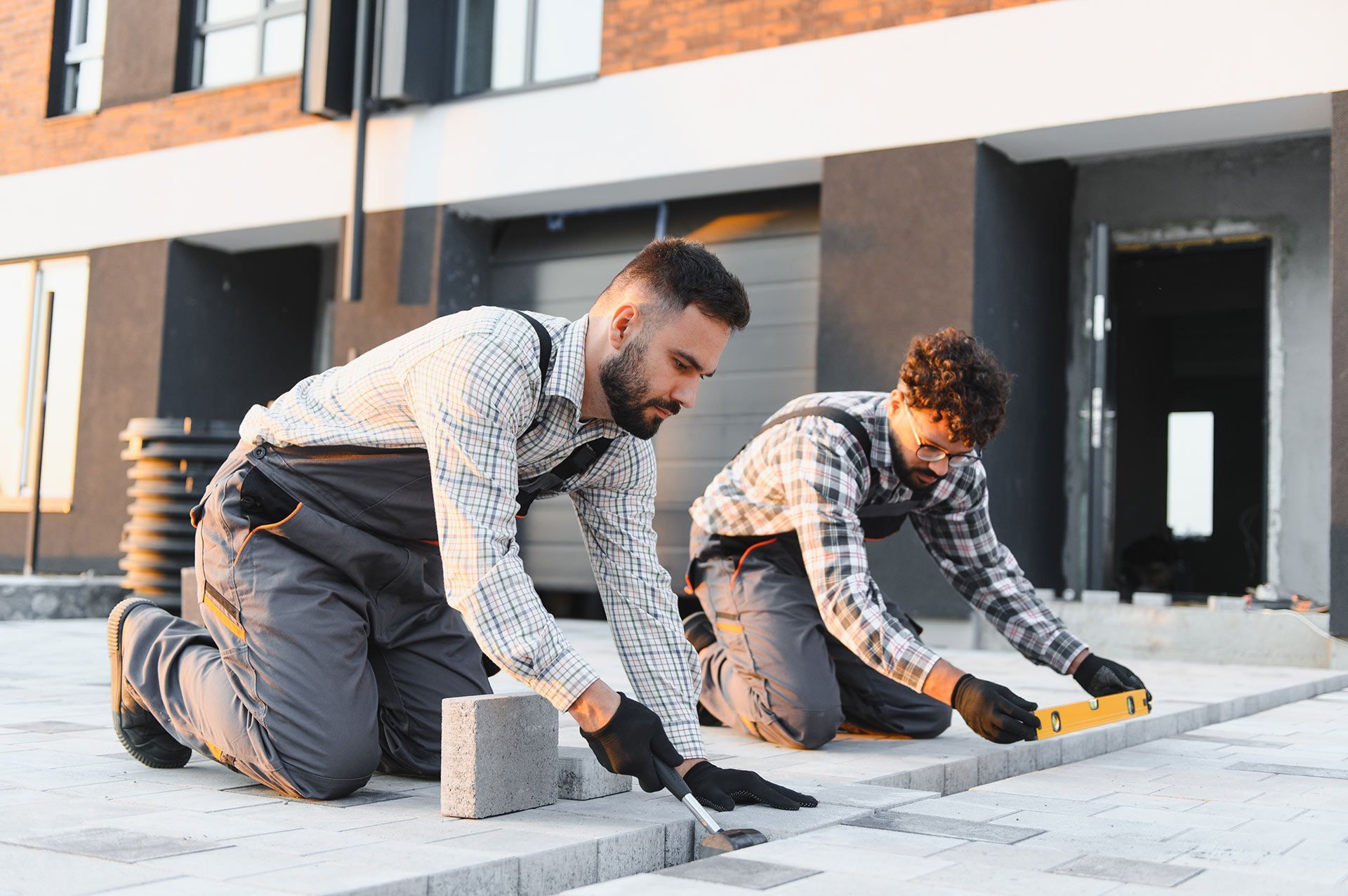 Two workers kneeling and smoothing concrete on a sidewalk beside a building