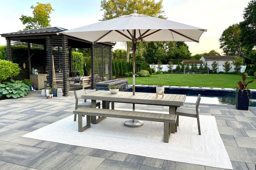 Patio with a picnic table under a large umbrella, overlooking a garden and a pergola