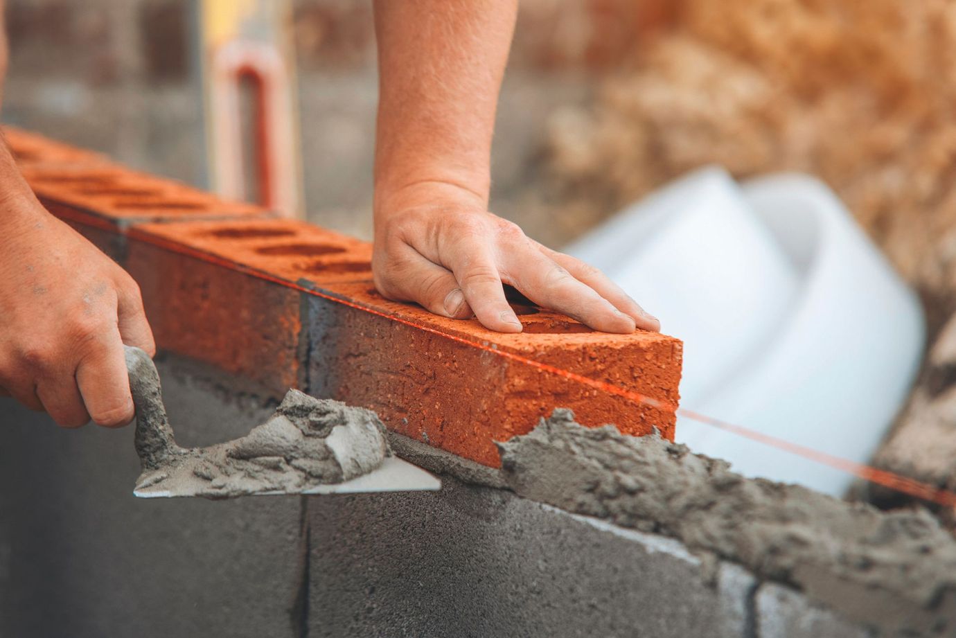 Hands laying gray mortar between orange bricks on a wall under construction