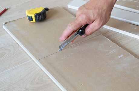 Picture of a drywall installer cutting drywall on the ground in preparation of a drywall repair.