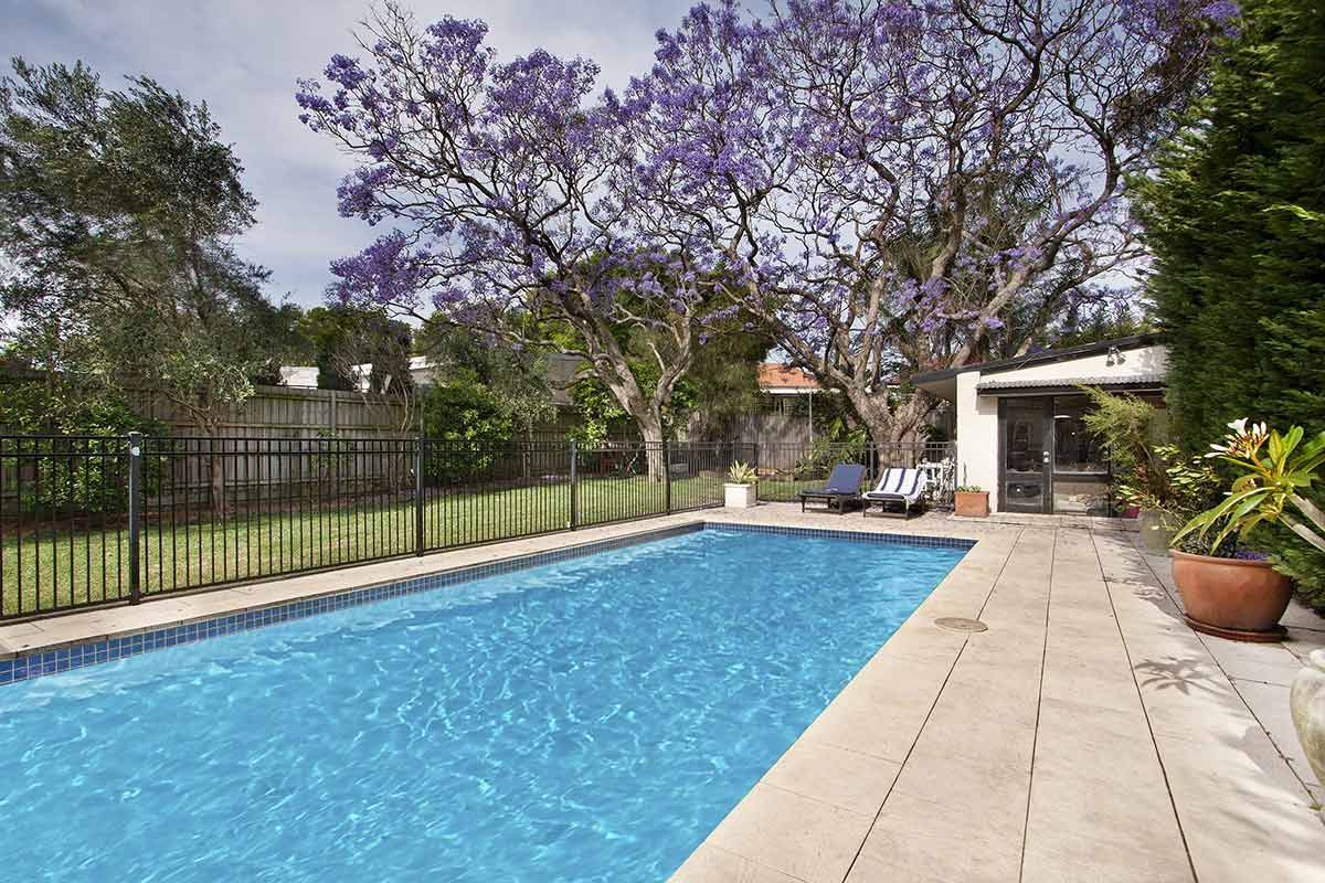 A arge Swimming Pool Is Surrounded by Trees and A Fence — Brendan's Landscaping and Fencing In Bundaberg, QLD