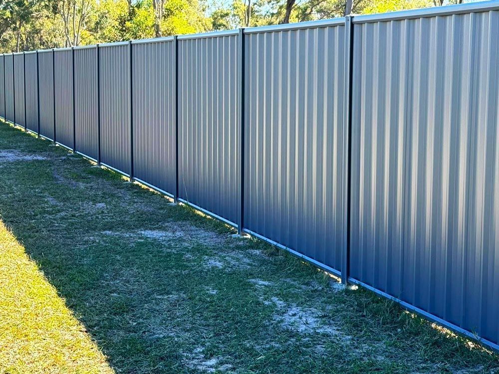 Blue Metal Fence is Sitting on Top of a Lush Green Field — Brendan's Landscaping and Fencing In Bundaberg, QLD