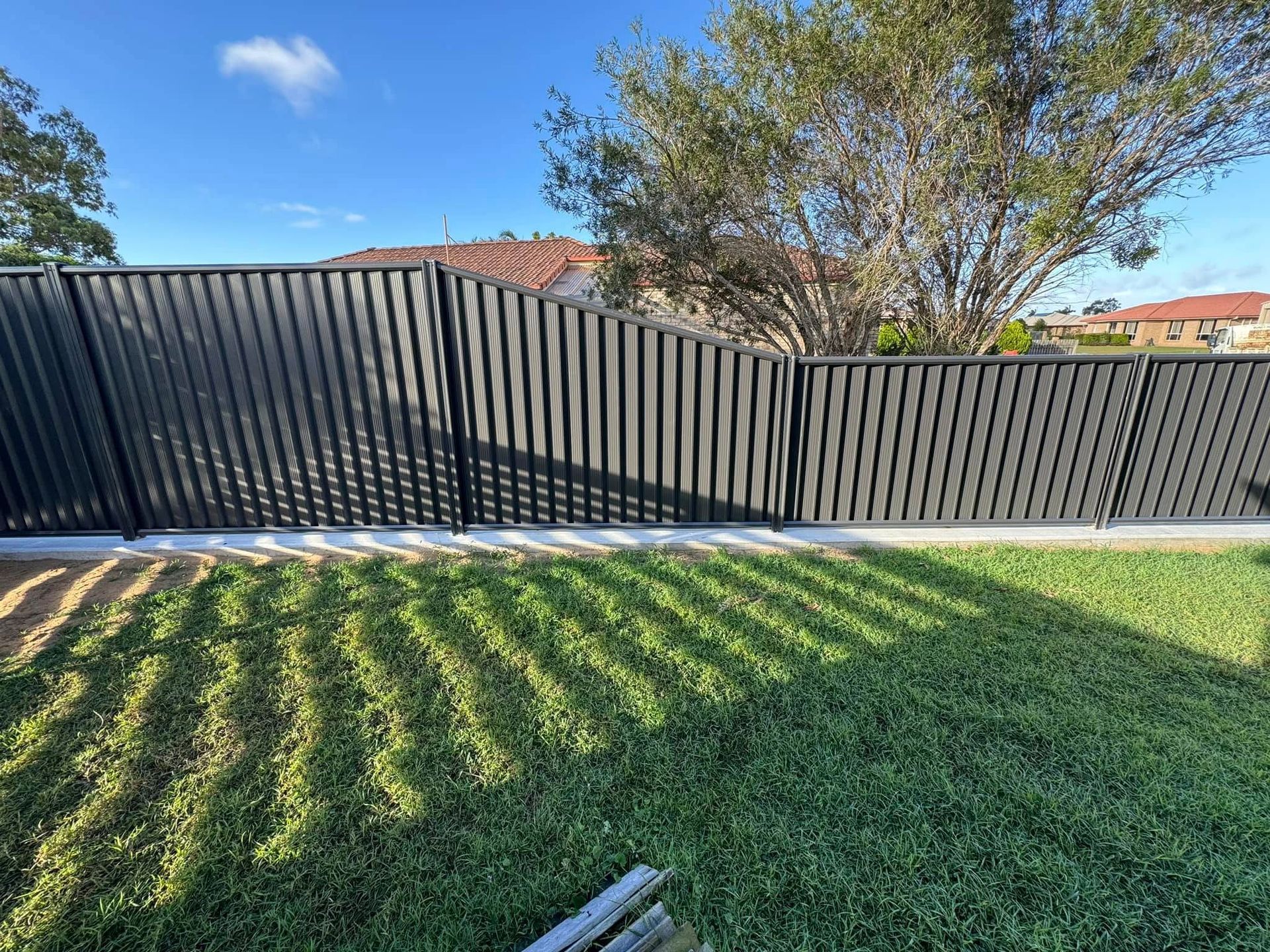 Black Slatted Fence Stands In Backyard On Grass
