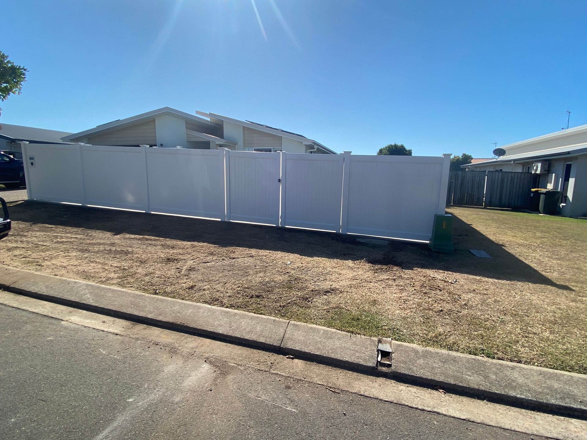 A White Vinyl Fence Surrounds a Lush Green Yard — Brendan's Landscaping and Fencing In Bundaberg, QLD