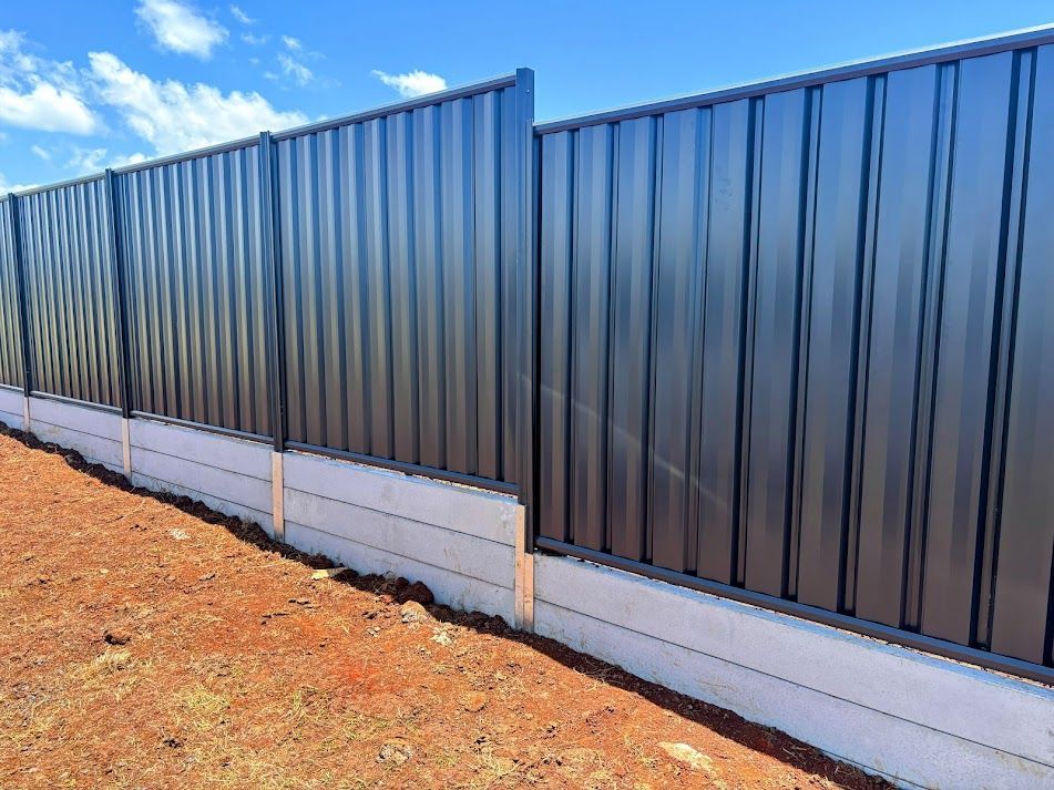 A Stone Wall With a Metal Fence Surrounding It — Brendan's Landscaping and Fencing In Bundaberg, QLD