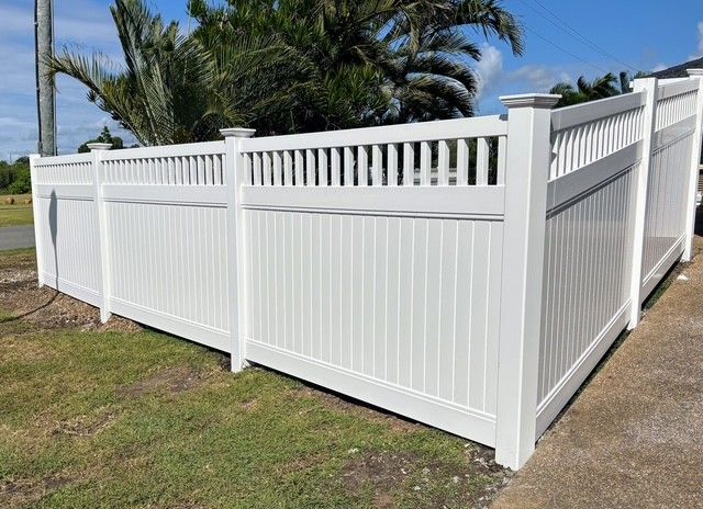 A White Fence is Sitting on Top of a Lush Green Field — Brendan's Landscaping and Fencing In Bundaberg, QLD