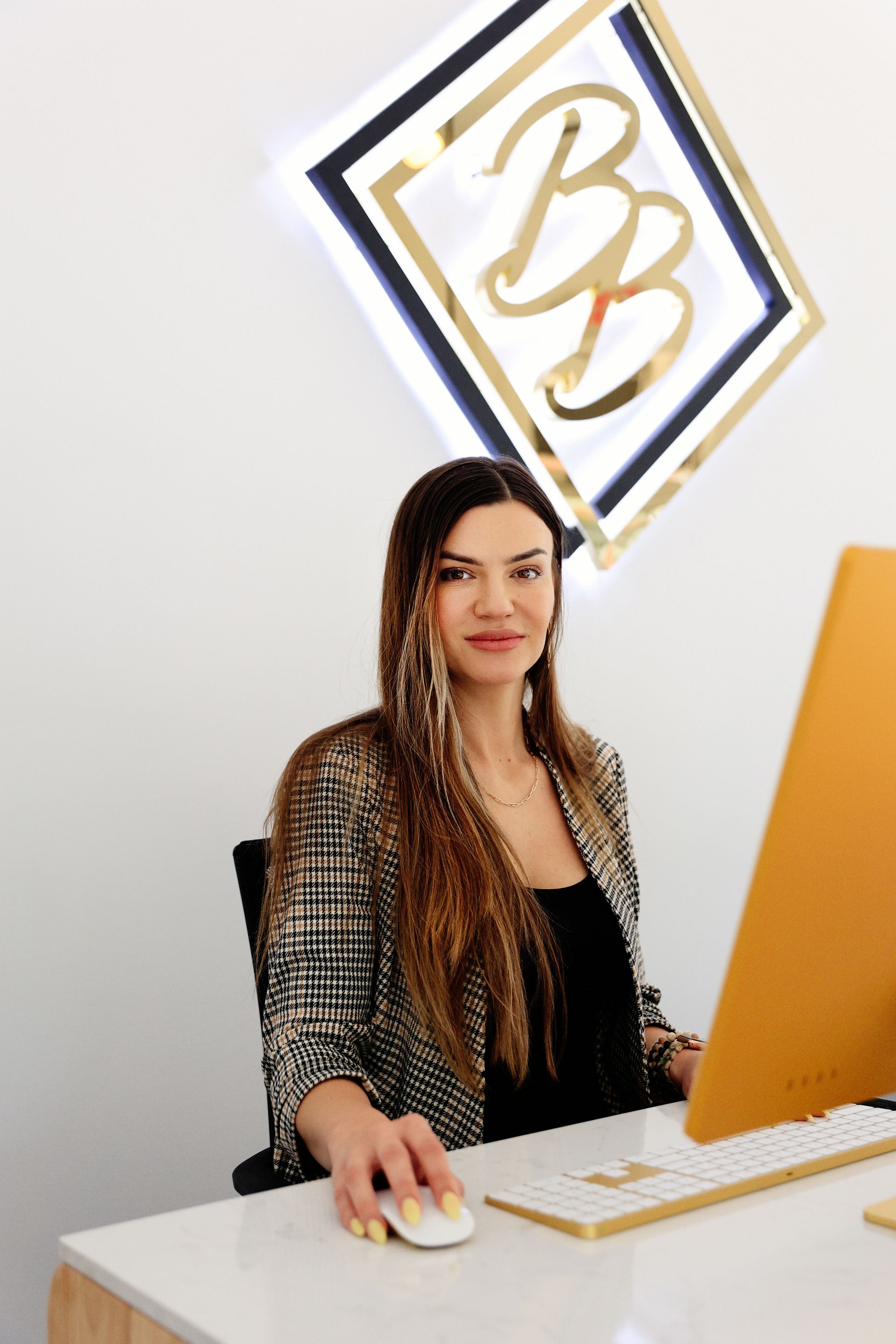 Woman seated at a desk using a computer in a modern office with a glowing wall logo