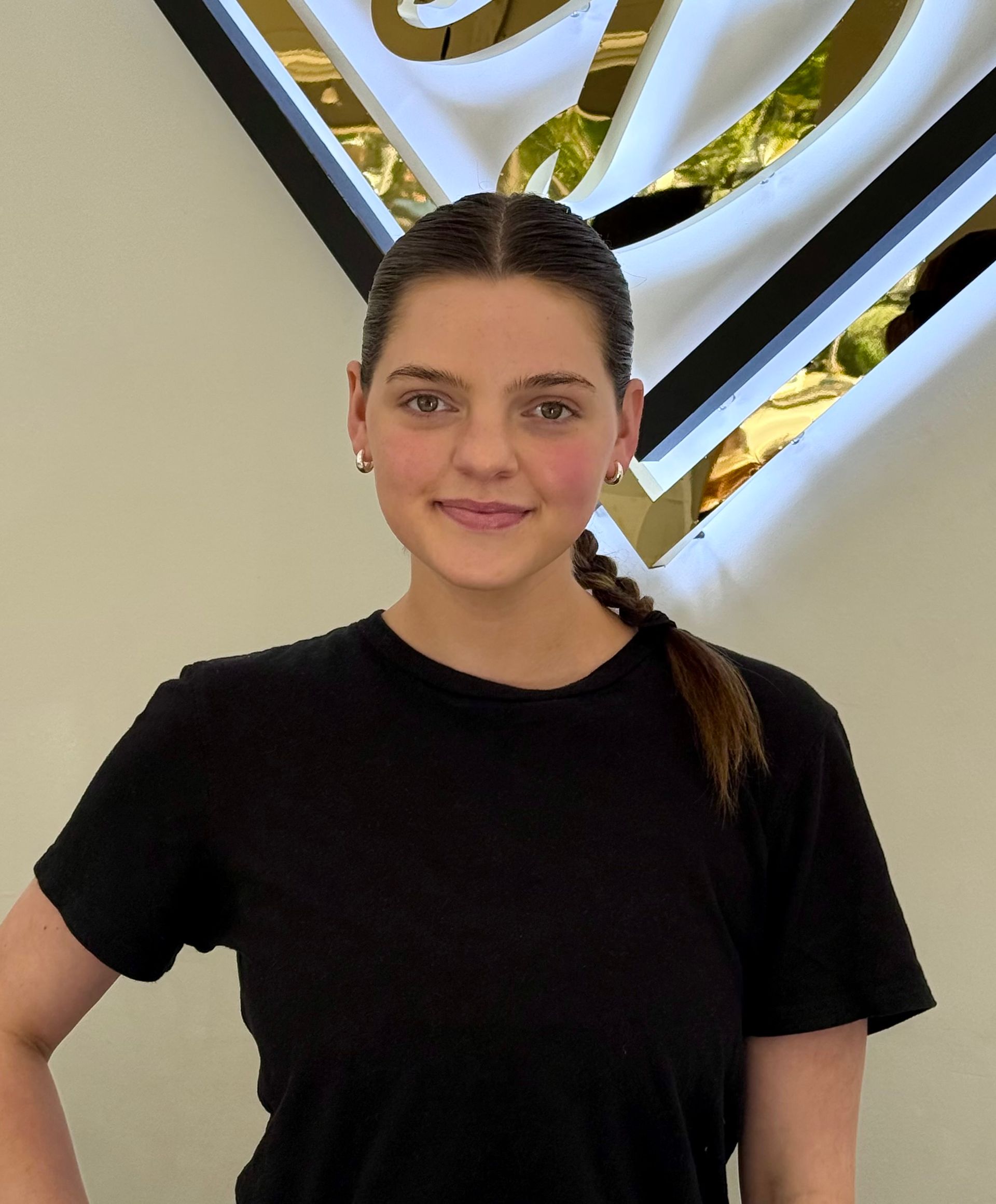 Woman in black shirt standing indoors beneath a glowing geometric wall sign