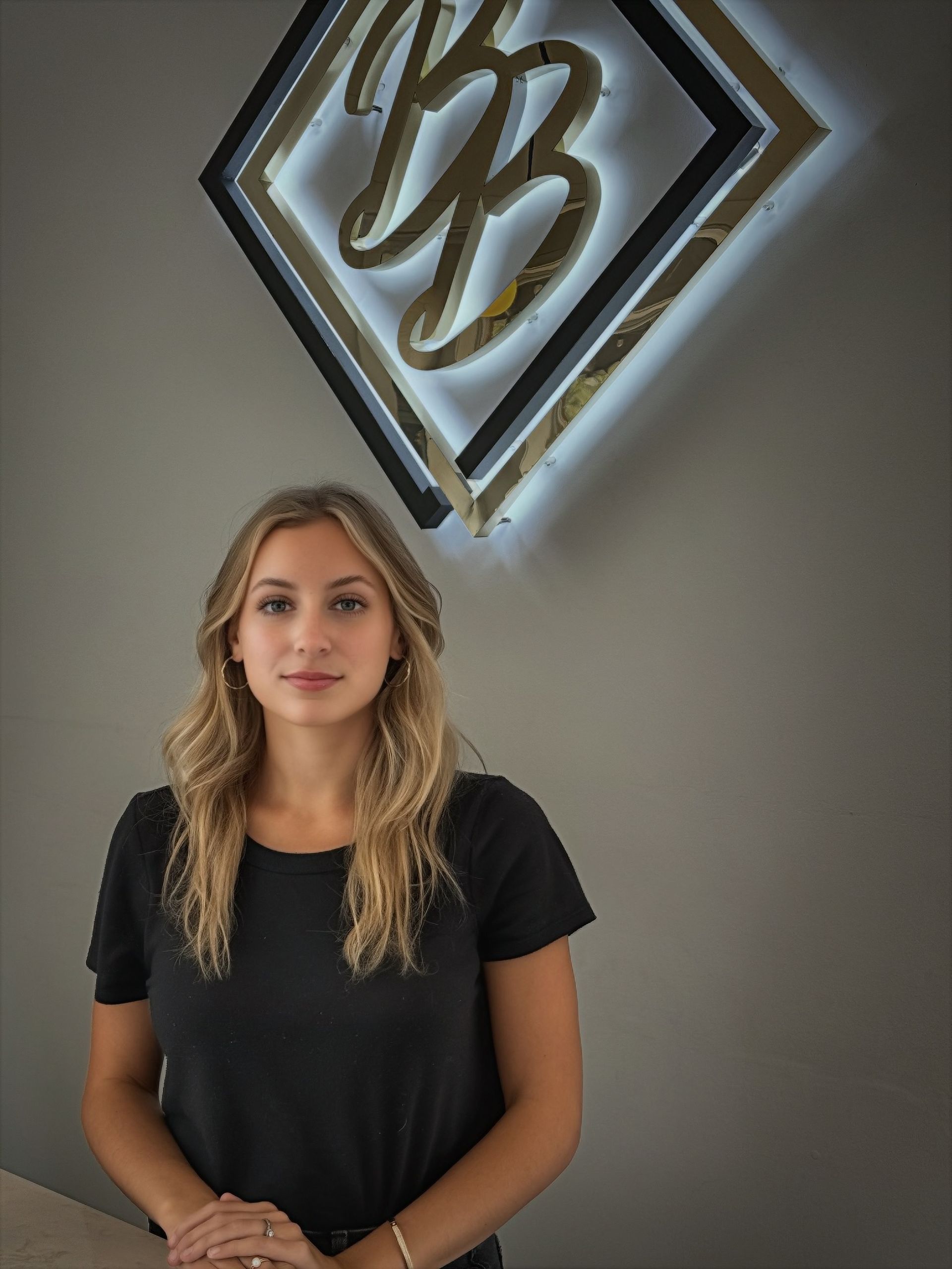 Woman in black shirt standing indoors beneath a glowing geometric wall sign