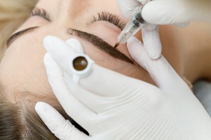 Gloved hands applying bright pink lip color to a closed-eyed face with a needle-like tool