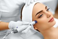 A clinician applies a handheld device to a woman’s cheek during a facial treatment.