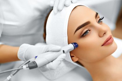 Cosmetic treatment with a gloved clinician using a handheld device on a woman’s face during a facial procedure