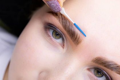 Gloved hands tattooing a woman's eyebrow with a handheld cosmetic tool