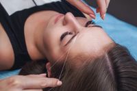 Person receiving eyebrow threading treatment with a close-up of the face and hands using thread