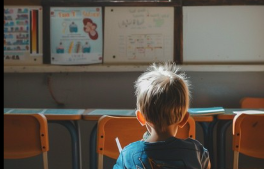 Child seated facing a classroom whiteboard with posters and chairs in a sunlit room