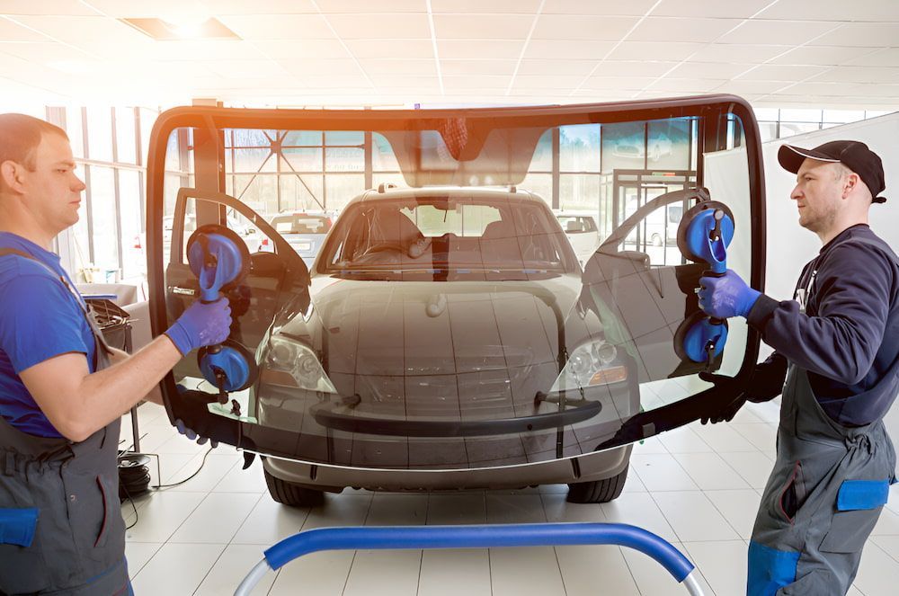 Two Men Are Installing A Windshield On A Car In A Garage — Canberra Windscreens In Conder, ACT