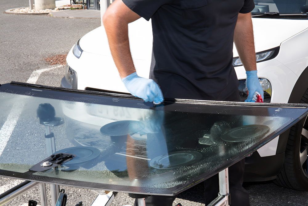 A Man Is Holding A Piece Of Glass In Front Of A Car — Canberra Windscreens In Weston Creek, ACT
