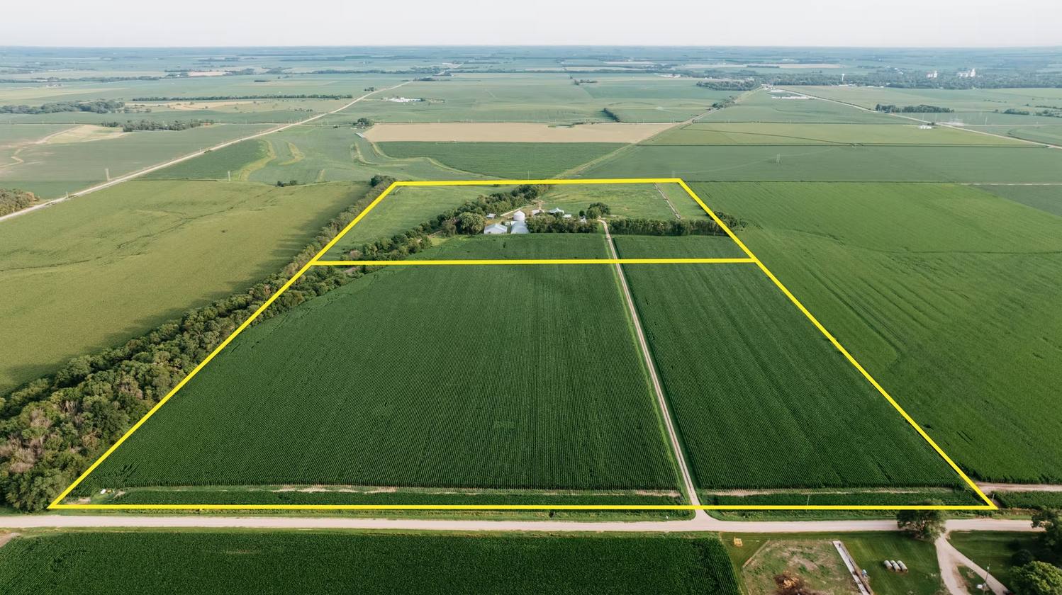 Aerial view of green agricultural fields outlined in yellow, with a small farmstead near the center.