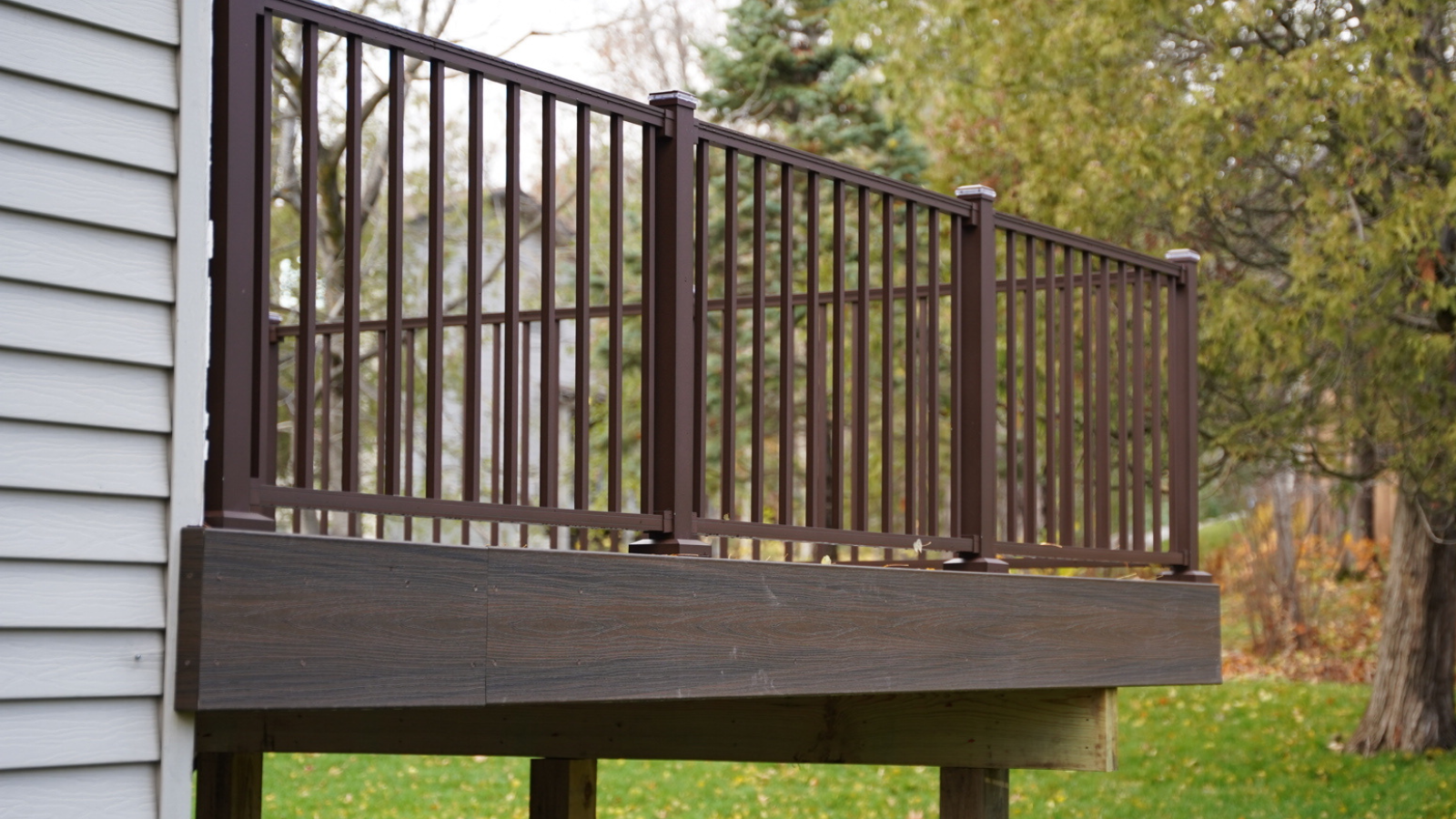 A deck with a brown railing is next to a house.